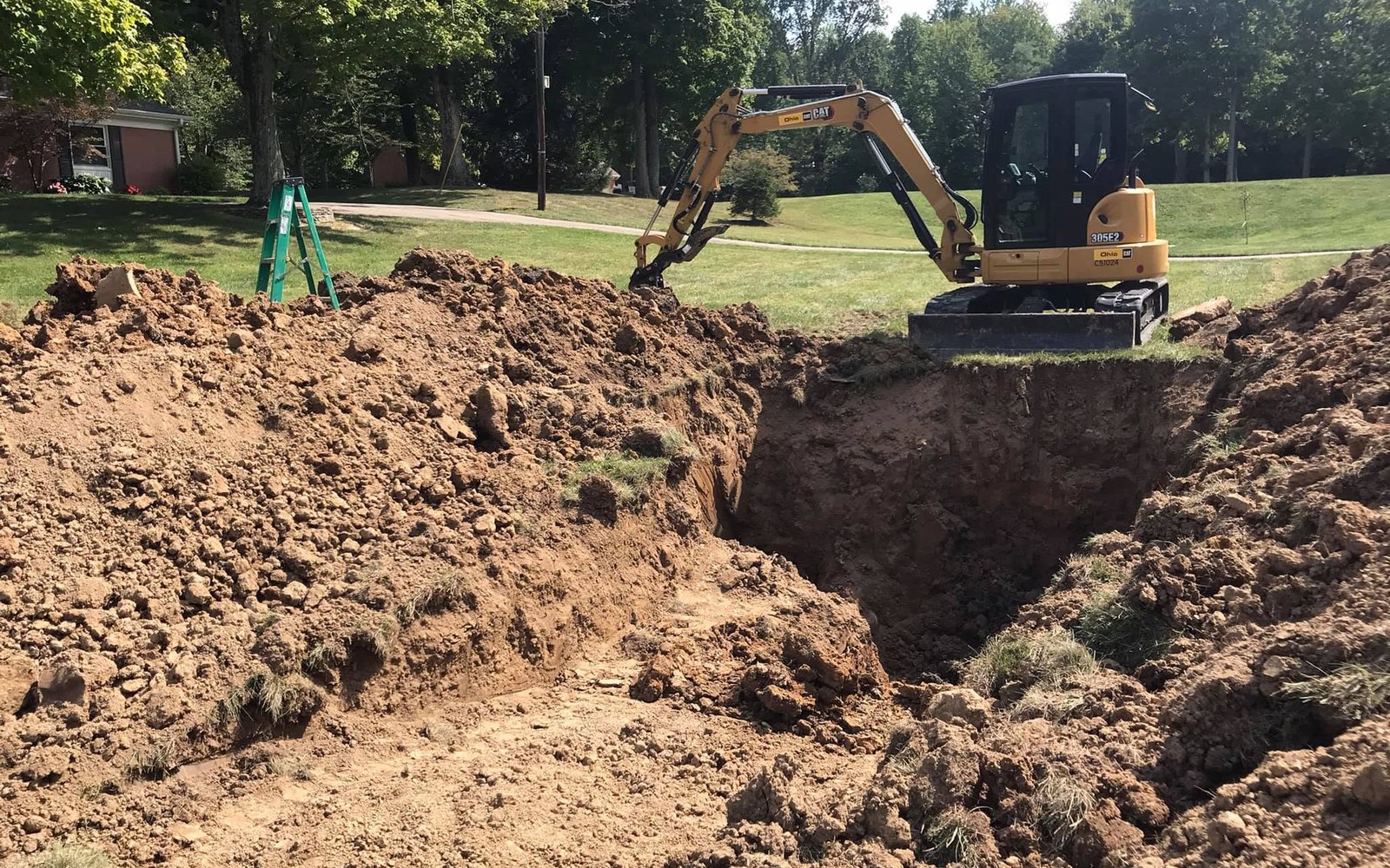 Compact excavator working beside a deep residential trench