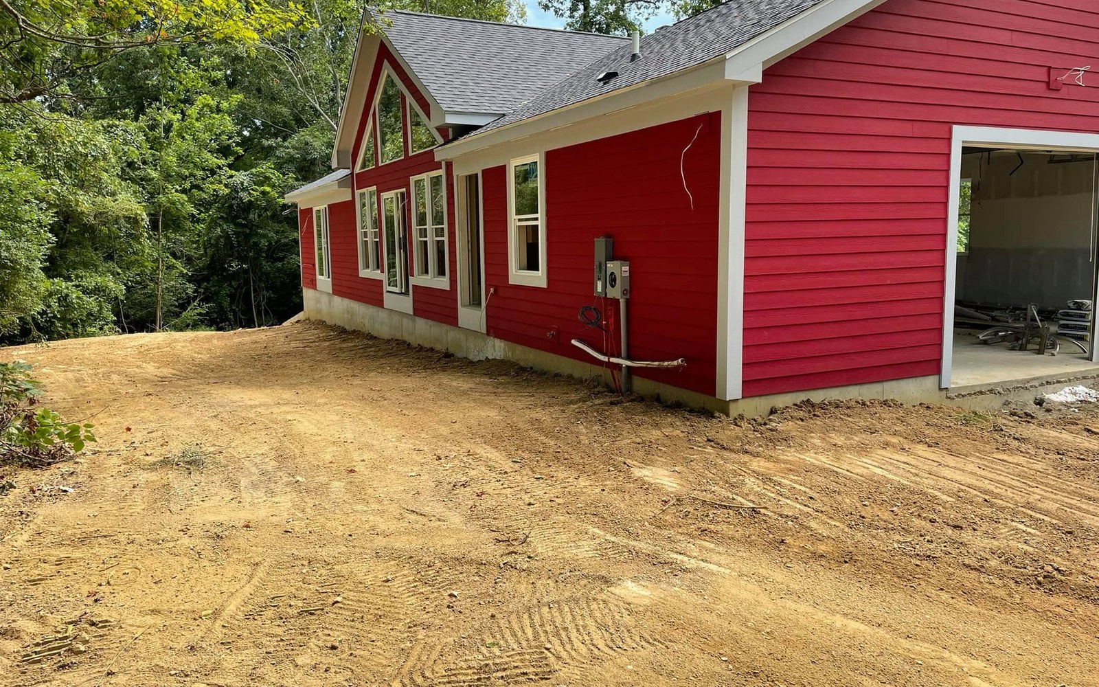 Prepared soil and machine tracks beside a completed red home