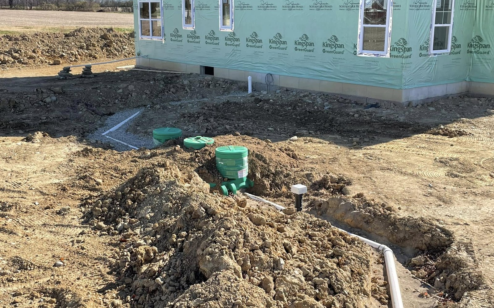 Green septic components and piping installed beside a home under construction